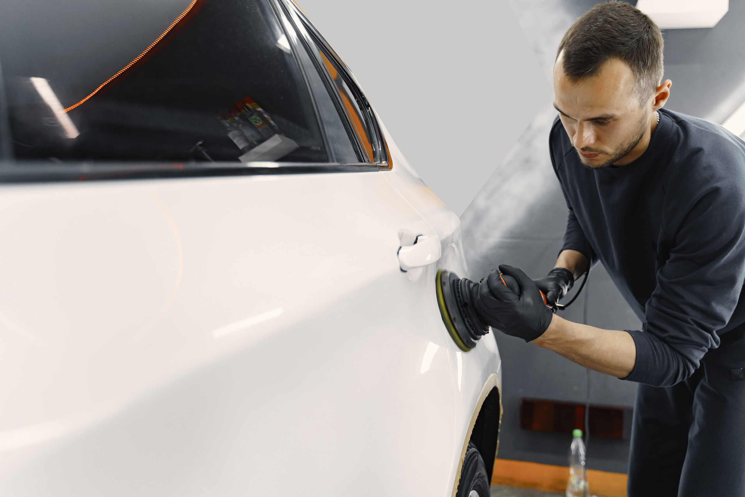 Man In A Garage. Worker Polish A Car. Man In A Black Uniform.